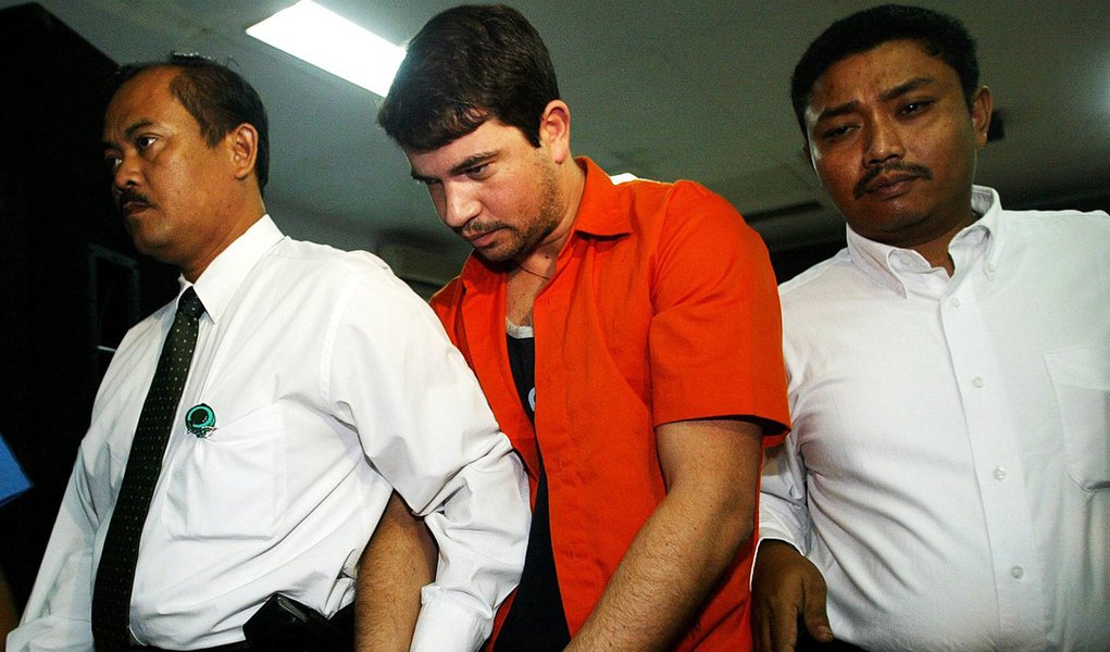 Rodrigo Gularte of Brazil, center, is escorted by plainclothed police officers as he is shown to the media at the Customs' office near the main airport in Jakarta, Indonesia, Thursday, Aug. 5, 2004. Gularte with two other Brazilians identified as Fred Syl