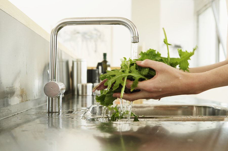 Young woman washing lettuce at kitchen sink, close-up of hands