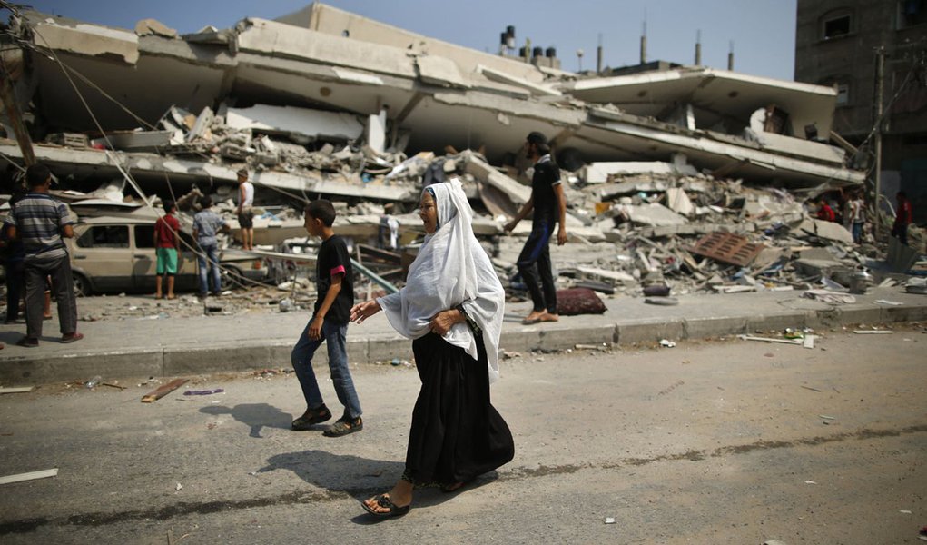 Palestinos caminham prÃ³ximos aos escombros de um prÃ©dio residencial que a polÃ­cia diz ter sido destruÃ­do em um ataque aÃ©reo de Israel, em Gaza. 22/07/2014.
 REUTERS/Mohammed Salem