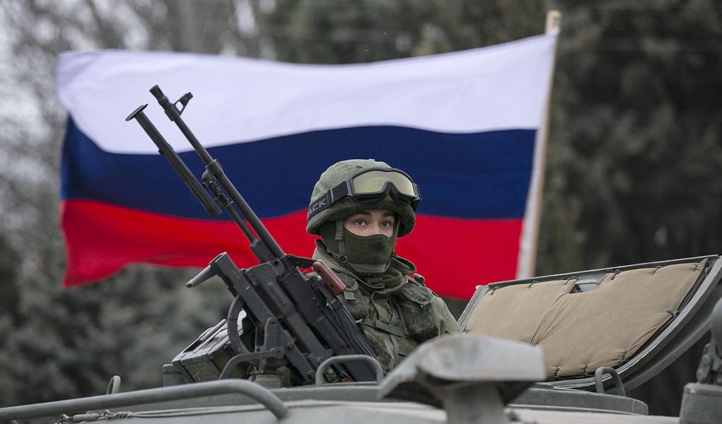 A pro-Russian man (not seen) holds a Russian flag behind an armed servicemen on top of a Russian army vehicle outside a Ukrainian border guard post in the Crimean town of Balaclava March 1, 2014. Ukraine accused Russia on Saturday of sending thousands of 