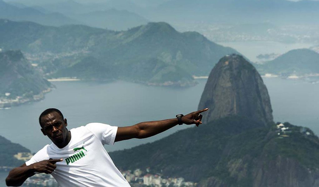 Fastest person ever Jamaicain Usain Bolt poses pointing at the Sugar Loaf mountain (back) under the Christ the Redeemer statue on Corcovado mountain  in Rio de Janeiro, Brazil on October 23, 2012. AFP PHOTO / Christophe Simon