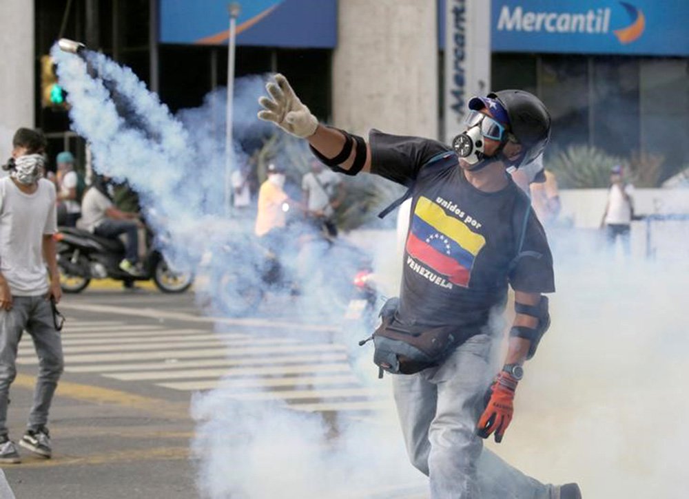 Manifestante de oposição arremessa de volta granada de gás lacrimogêneo lançada pela polícia durante protesto. 19/04/2017 REUTERS/Marco Bello
