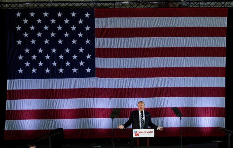 U.S. President-elect Donald Trump speaks beneath a giant American Flag during a "Thank You USA" tour rally in Baton Rouge, Louisiana, U.S., December 9, 2016. REUTERS/Mike Segar