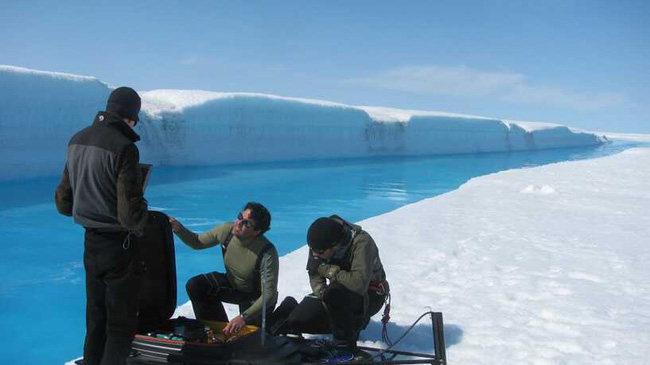 Cientistas na borda de um rio formado por gelo derretido, na Groenlândia