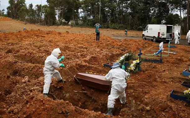 Coveiros vestindo roupas de proteção se preparam para enterrar no cemitério Parque Taruma, em Manaus.