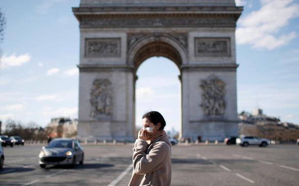 Uma mulher usando uma máscara protetora caminha perto do Arco do Triunfo, em Paris
