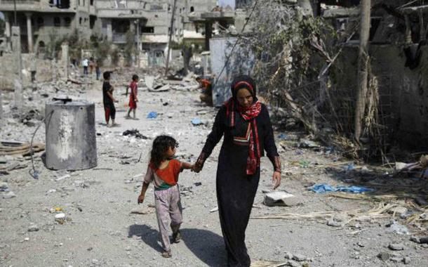 Palestina caminha com criança por prédios destruídos ao norte da Faixa de Gaza