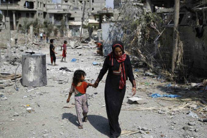Palestina caminha com criança por prédios destruídos ao norte da Faixa de Gaza