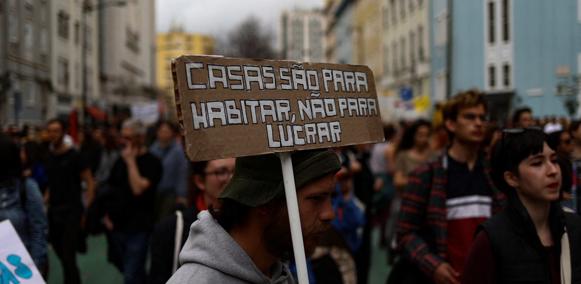 Um homem carrega um cartaz enquanto pessoas se manifestam pelo direito à habitação acessível em Lisboa, Portugal, 1 de abril de 2023