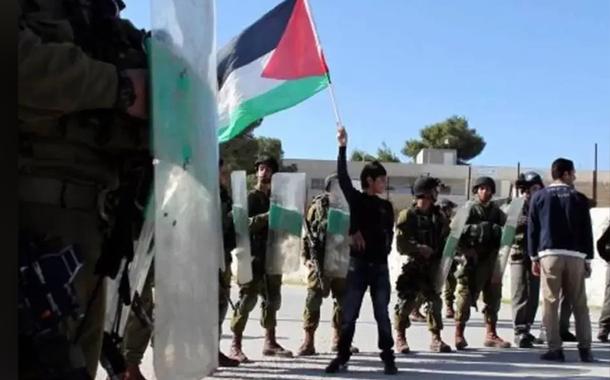 Jovem ergue bandeira da Palestina diante de militares de Israel