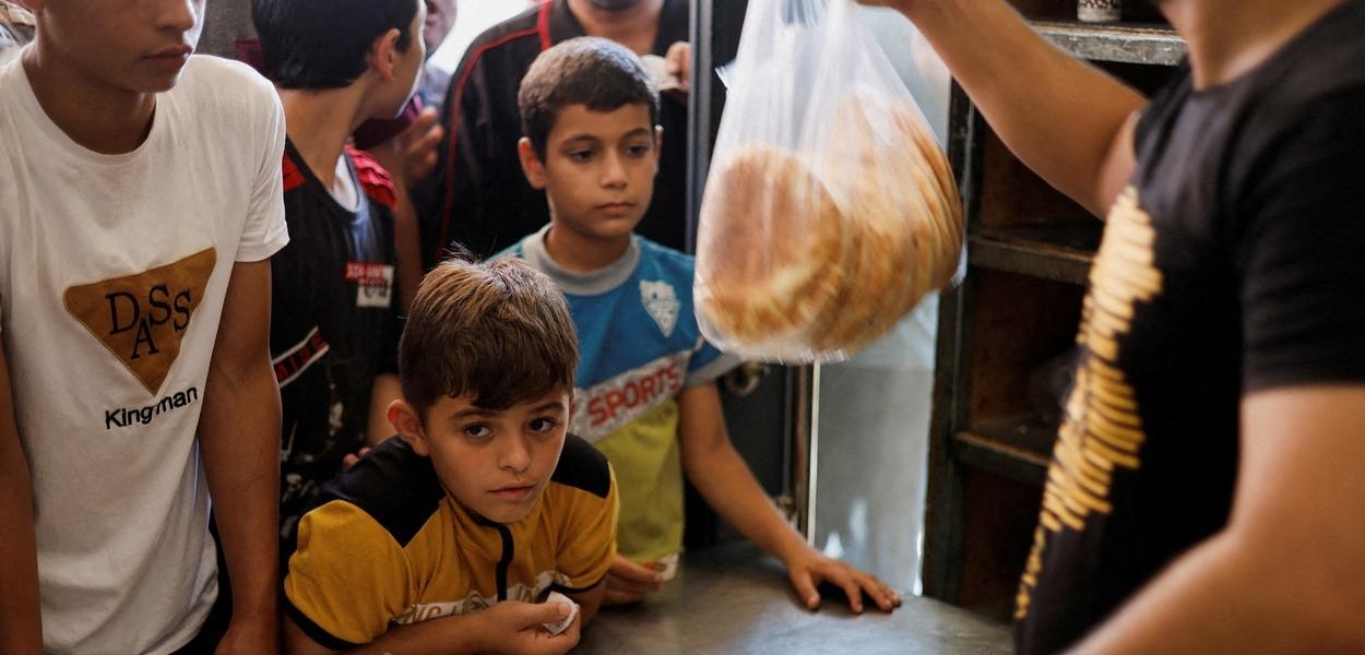 Palestinos esperam para comprar pão do lado de fora de uma padaria, em meio ao conflito em curso entre Israel e o grupo islâmico palestino Hamas, em Khan Younis, no sul da Faixa de Gaza