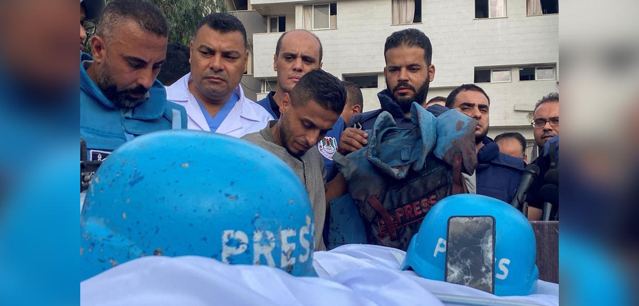 Colegas dos jornalistas palestinos Mohammed Sobh e Saeed al-Taweel, que foram mortos quando um míssil israelense atingiu um prédio próximo, estão ao lado de seus corpos em um hospital na cidade de Gaza, em 10 de outubro de 2023. Um colega também é visto segurando o colete à prova de balas usado por um dos homens falecidos