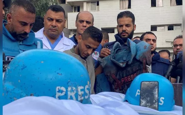Colegas dos jornalistas palestinos Mohammed Sobh e Saeed al-Taweel, que foram mortos quando um míssil israelense atingiu um prédio próximo, estão ao lado de seus corpos em um hospital na cidade de Gaza, em 10 de outubro de 2023. Um colega também é visto segurando o colete à prova de balas usado por um dos homens falecidos