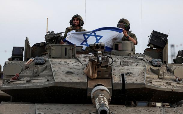 Soldados israelenses seguram bandeira israelense em um tanque perto da fronteira de Israel com a Faixa de Gaza