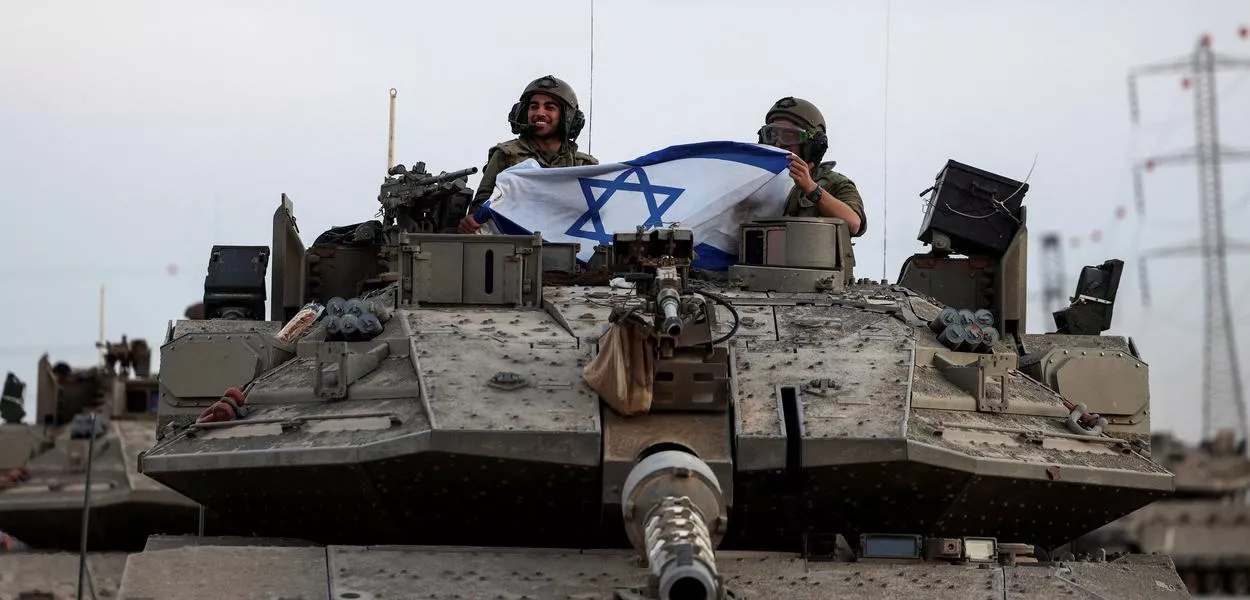 Soldados israelenses seguram bandeira israelense em um tanque perto da fronteira de Israel com a Faixa de Gaza