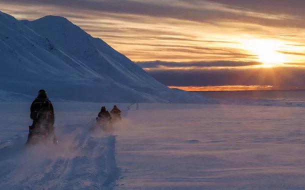 Cientistas dirigem seus veículos para neve cruzando o Ártico em direção a Kongsfjord durante o pôr do sol perto de Ny-Alesund, Svalbard, Noruega, 10 de abril de 2023