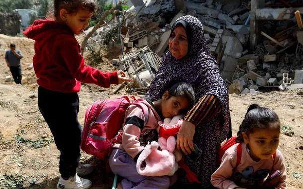 Uma mulher palestina, Fatima Bashir, e suas netas sentam-se ao lado dos restos de sua casa, que foi destruída em ataques aéreos israelenses