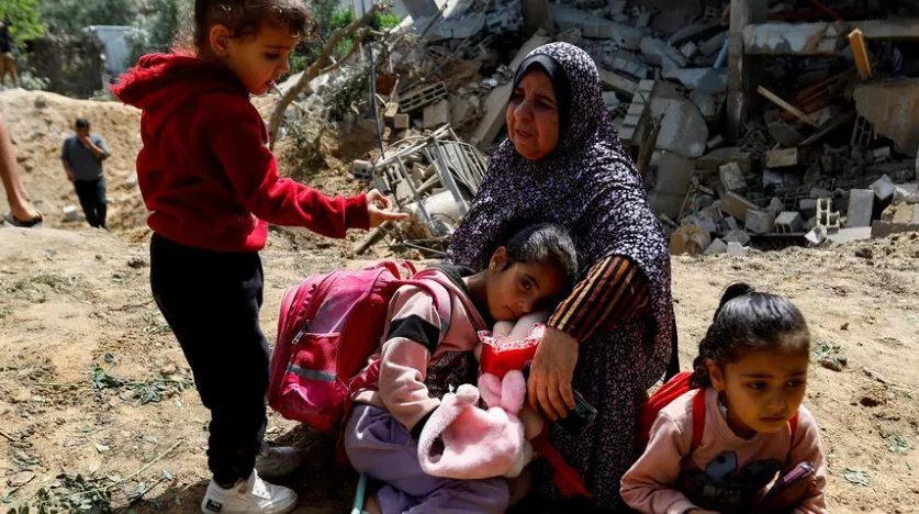 Uma mulher palestina, Fatima Bashir, e suas netas sentam-se ao lado dos restos de sua casa, que foi destruída em ataques aéreos israelenses
