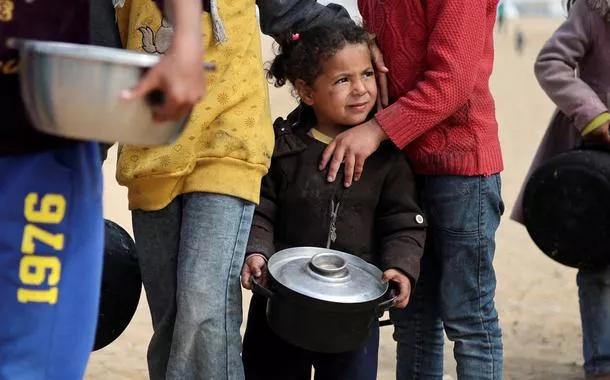 Crianças palestinas deslocadas esperam para receber comida em um acampamento, em meio à escassez de alimentos na Faixa de Gaza