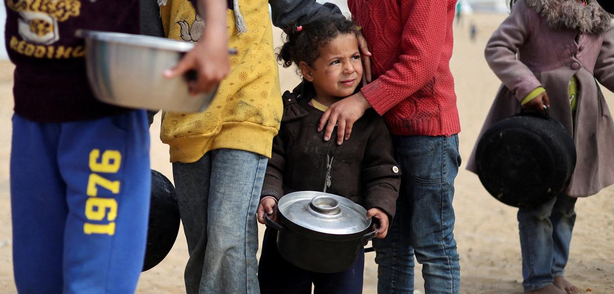 Crianças palestinas deslocadas esperam para receber comida em um acampamento, em meio à escassez de alimentos na Faixa de Gaza