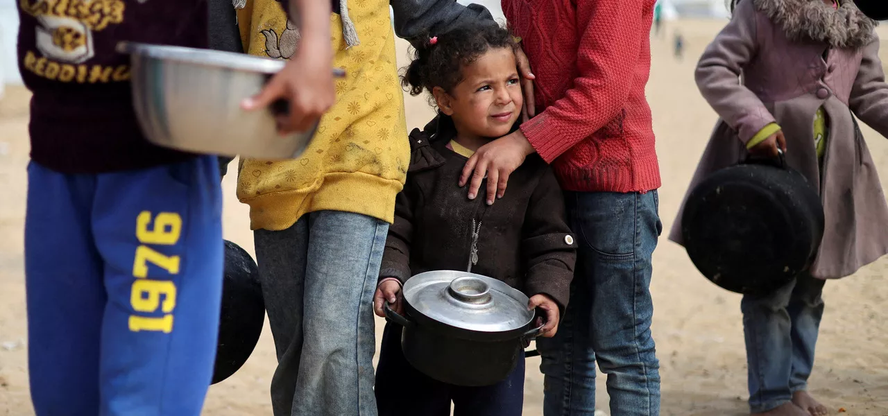 Crianças palestinas deslocadas esperam para receber comida em um acampamento, em meio à escassez de alimentos na Faixa de Gaza