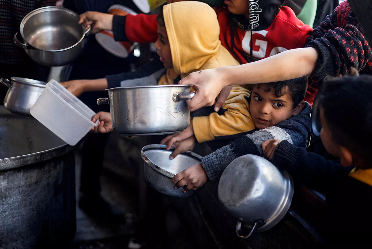 Crianças palestinas esperam comida preparada em cozinha de caridade em meio à escassez de alimentos, em Rafah, na Faixa de Gaza