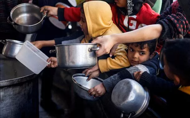 Crianças palestinas esperam comida preparada em cozinha de caridade em meio à escassez de alimentos, em Rafah, na Faixa de Gaza