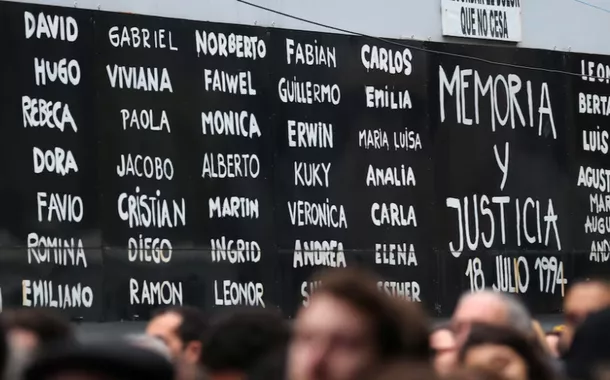 Pessoas ficam em frente a uma placa que diz "Memória e Justiça" ao lado dos nomes das vítimas do atentado à bomba na Associação Mútua Israelita Argentina (AMIA) em 1994, durante as comemorações do 24º aniversário do ataque em Buenos Aires, Argentina, em 18 de julho de 2018