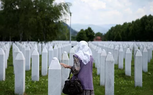 Uma mulher muçulmana bósnia toca uma lápide no Memorial do Genocídio de Srebrenica em Potocari, Bósnia e Herzegovina, 8 de junho de 2021