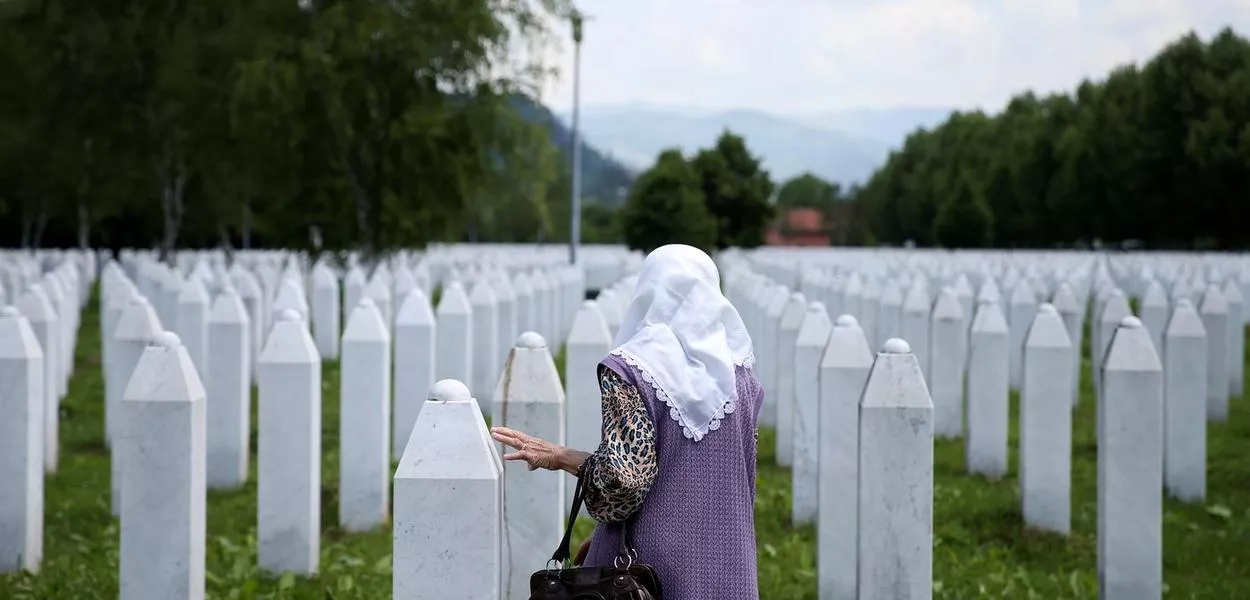 Uma mulher muçulmana bósnia toca uma lápide no Memorial do Genocídio de Srebrenica em Potocari, Bósnia e Herzegovina, 8 de junho de 2021