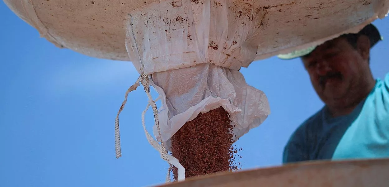 Trabalhador agrícola carrega trator com fertilizante, perto de Brasília (DF)