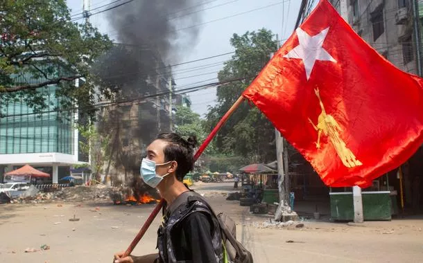 Um homem segura uma bandeira da Liga Nacional para a Democracia durante um protesto contra o golpe militar, em Yangon, Mianmar, 27 de março de 2021