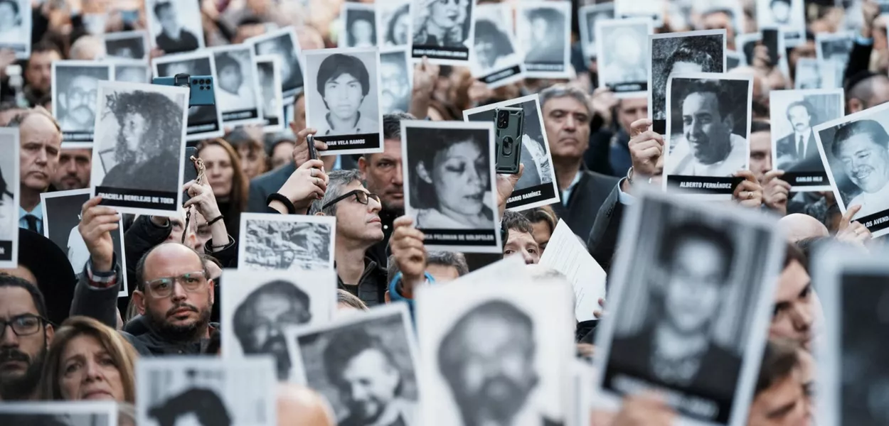 Pessoas seguram imagens das vítimas do ataque a bomba de 1994 no centro comunitário da Associação Mútua Israelita Argentina (AMIA), marcando o 30º aniversário do ataque, em Buenos Aires, Argentina, 18 de julho de 2024