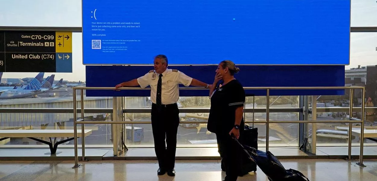 Funcionários da United Airlines aguardam perto de um monitor de voos exibindo uma tela azul de erro, no Terminal C do Aeroporto Internacional de Newark, Nova Jersey