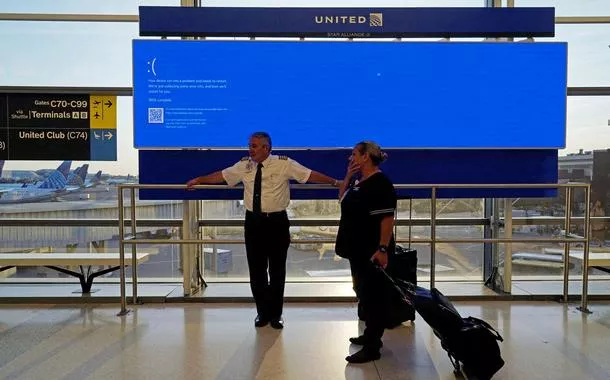 Funcionários da United Airlines aguardam perto de um monitor de voos exibindo uma tela azul de erro, no Terminal C do Aeroporto Internacional de Newark, Nova Jersey