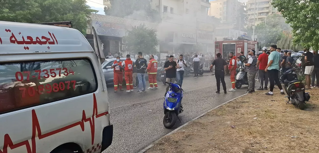 Fumaça sobe de uma loja móvel enquanto membros da defesa civil se reúnem em Sidon, Líbano, 18 de setembro de 2024