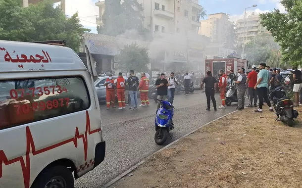 Fumaça sobe de uma loja móvel enquanto membros da defesa civil se reúnem em Sidon, Líbano, 18 de setembro de 2024