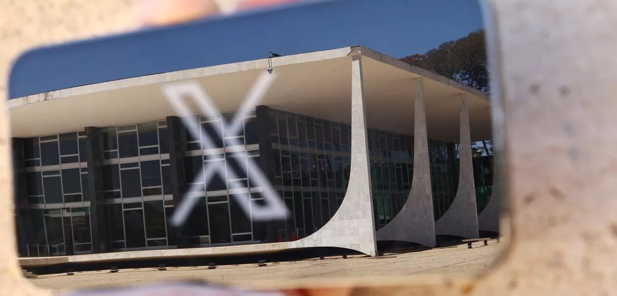 Logo da rede social X exibida em celular com reflexo do prédio do STF em Brasília
