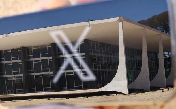 Logo da rede social X exibida em celular com reflexo do prédio do STF em Brasília