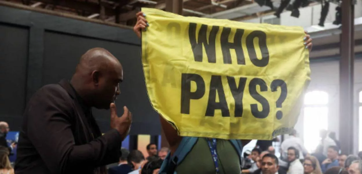 Ativista segura faixa com a frase 'Who pays?'