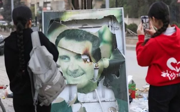 Mulheres tiram fotos de uma imagem danificada do presidente sírio Bashar al-Assad