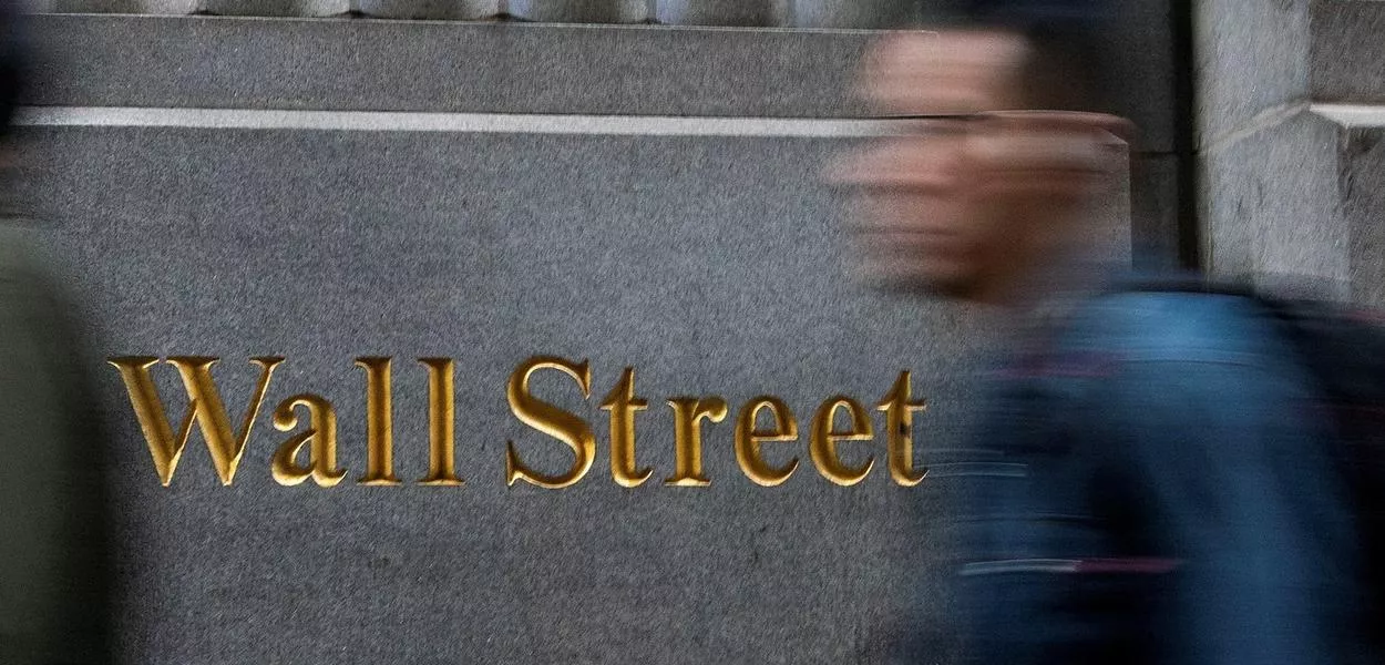Homem passa em frente a sinalização de Wall Street, em Nova York, EUA - 29/12/2023