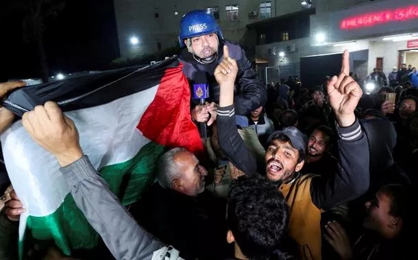 Palestinos que comemoram notícias sobre um cessar-fogo com Israel carregam o correspondente da Al Jazeera Ashraf Amrah, enquanto ele relata ao vivo em Deir Al-Balah, no centro da Faixa de Gaza