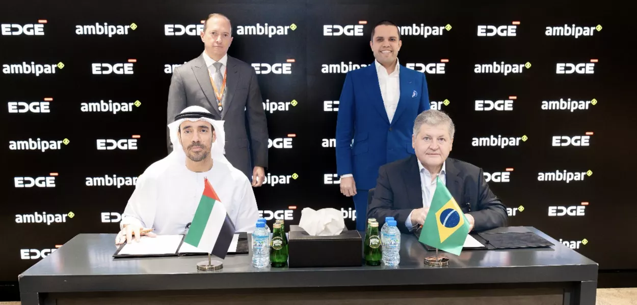 Presidente de negócios da EDGE, Omar Al Zaabi, e o CEO da Ambipar, Tercio Borlenghi Júnior, sentados na mesa. Em pé, estão Miles Chambers, da Edge, e Rodrigo Paiva, da Ambipar