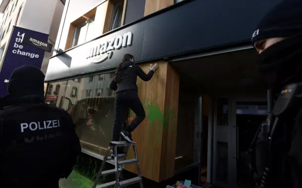 A polícia suíça fica em frente a um espaço da Amazon enquanto uma mulher limpa a vitrine depois que ativistas pintaram sua fachada com spray durante um protesto no dia de abertura da 55ª reunião anual do Fórum Econômico Mundial (WEF) em Davos, Suíça , 20 de janeiro de 2025