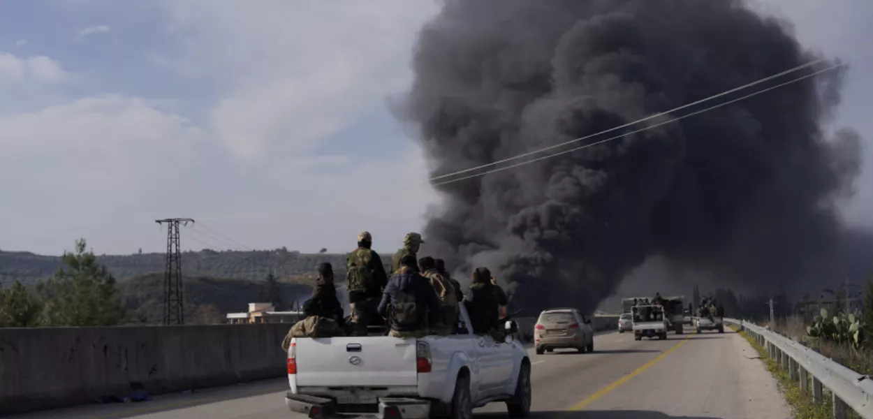 Fumaça sobe enquanto membros das novas forças regulares sírias viajam em um veículo enquanto lutam contra uma insurgência incipiente de combatentes aliados ao líder deposto Bashar al-Assad, em Latakia, Síria, 7 de março de 2025