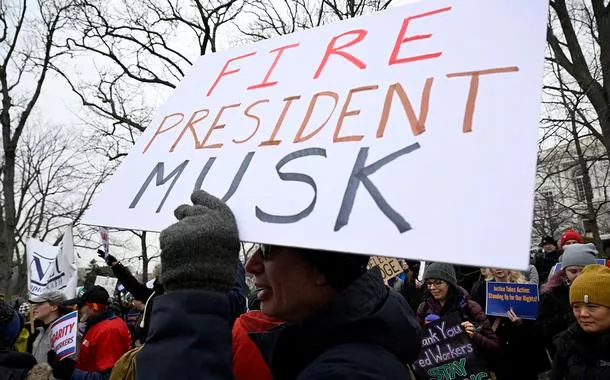 Manifestante com cartaz fazendo referência a Elon Musk, que lidera a iniciativa do presidente dos EUA, Donald Trump, para reduzir o tamanho do governo federal, enquanto ativistas de sindicatos trabalhistas se reúnem em apoio aos trabalhadores federais durante protesto no Capitólio, em Washington
