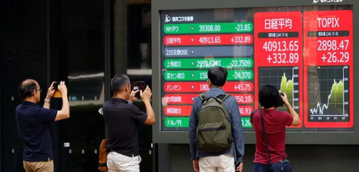 Pessoas tiram fotos de um monitor que exibe a média de ações Topix e a média de ações Nikkei do lado de fora de uma corretora em Tóquio