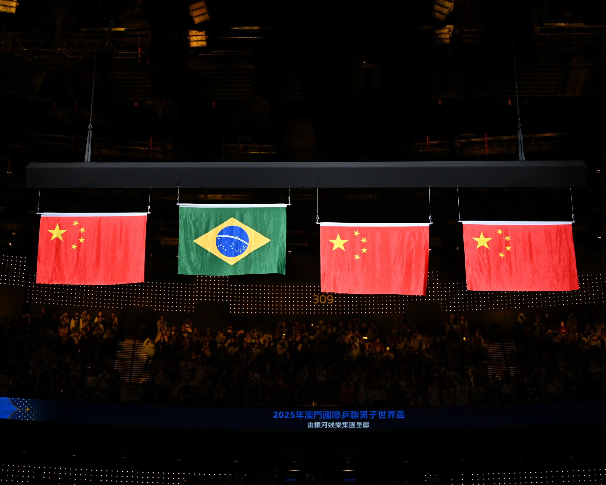 Bandeira do Brasil em destaque em meio a três bandeiras da China no pódio da Copa do Mundo de Tênis de Mesa de 2025, em Macau