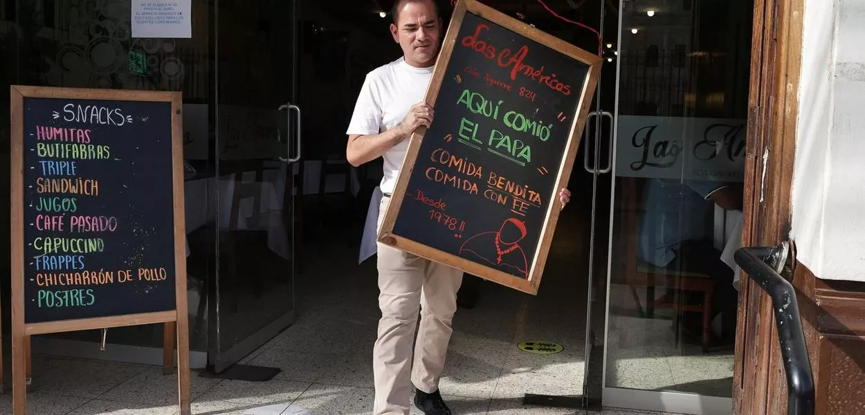 Homem segura quadro que diz: "O Papa comeu aqui. Comida abençoada, comida com fé", do lado de fora do restaurante "Las Américas", em Chiclayo - 09/05/2025